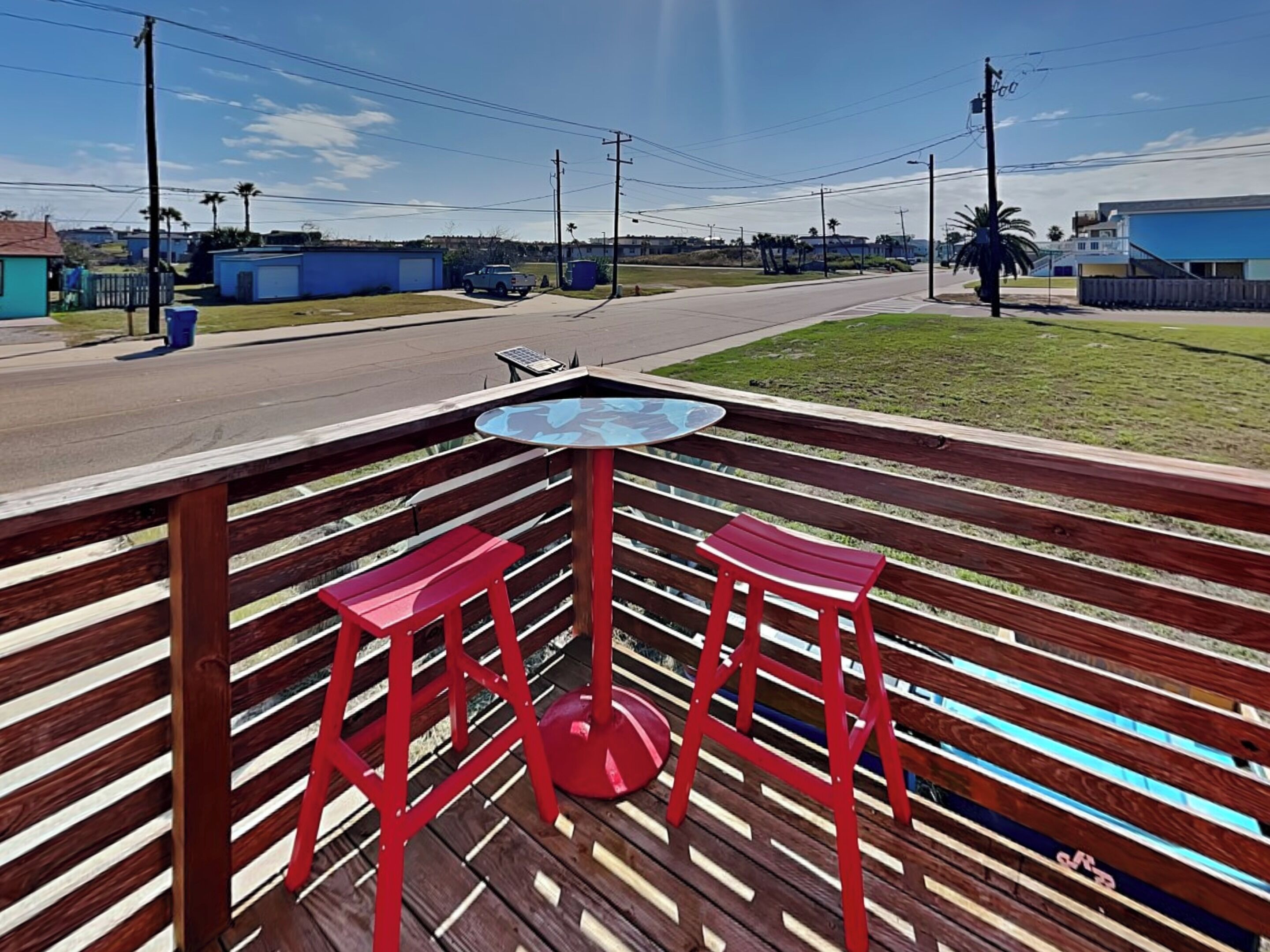Une terrasse en bois avec une table en verre et deux tabourets rouges.