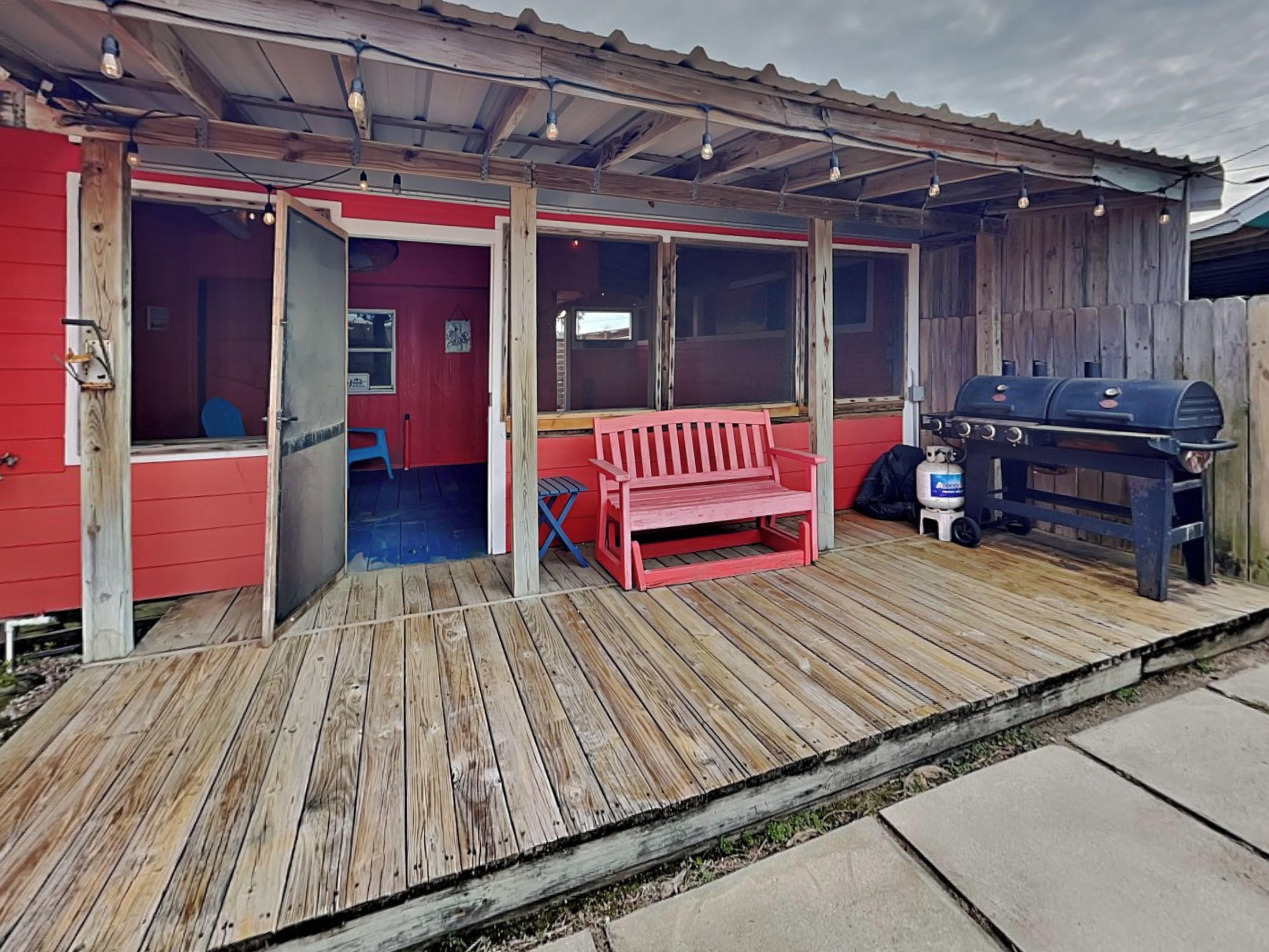 Una terraza de madera con un banco rojo y una parrilla.