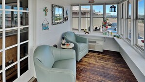 Um quarto com duas poltronas verde-claras, uma mesinha redonda com uma abacaxi e um carrinho de brinquedo, e um assento junto à janela com objetos decorativos.