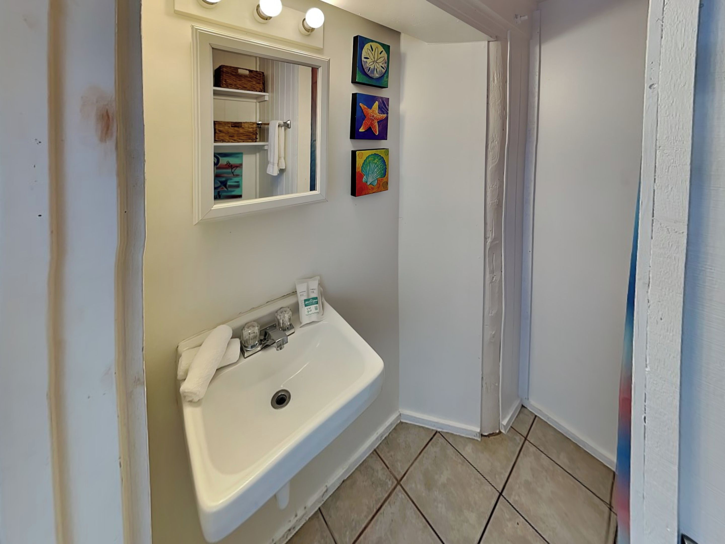 A bathroom with a white sink, a mirror, and three framed pictures on the wall.