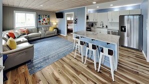 Uma cozinha moderna com eletrodomésticos de aço inoxidável, uma ilha central com banquetas e um espaço de jantar com sofá e mesa de centro.