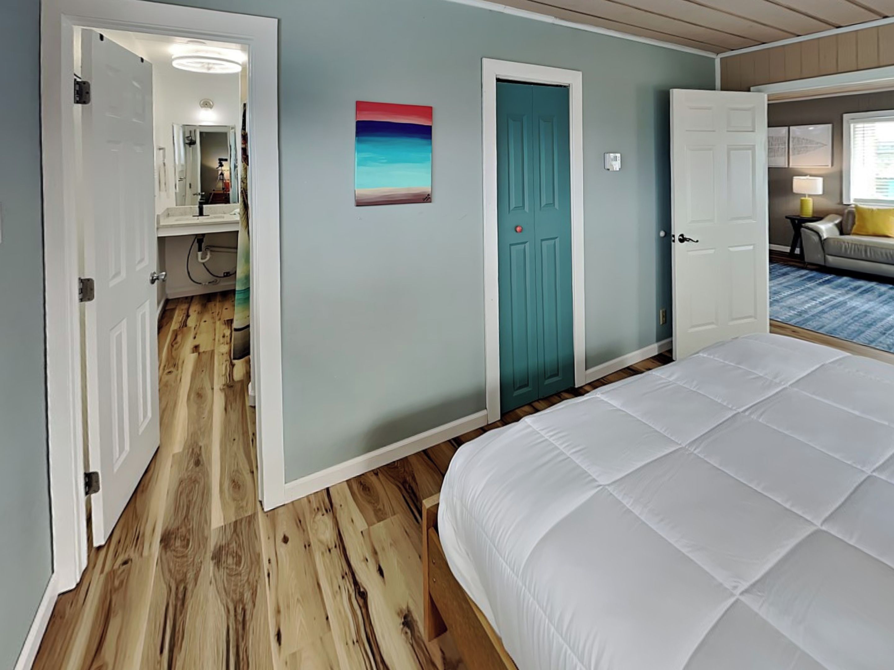 Ein Schlafzimmer mit Holzboden, einem Bett, einer Tür und einem Bild an der Wand.
