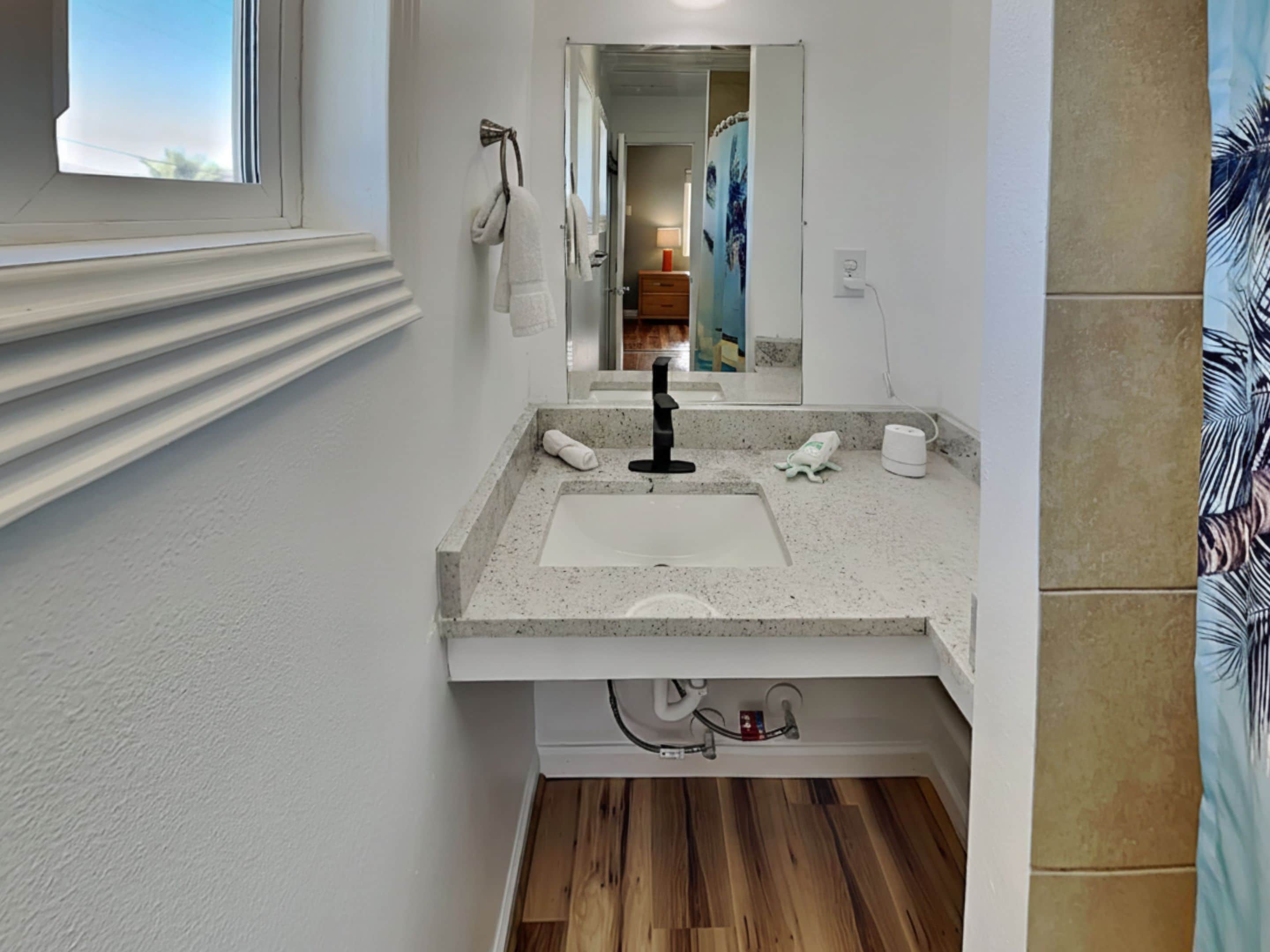 A bathroom with a sink, mirror, towel rack, and wooden flooring.