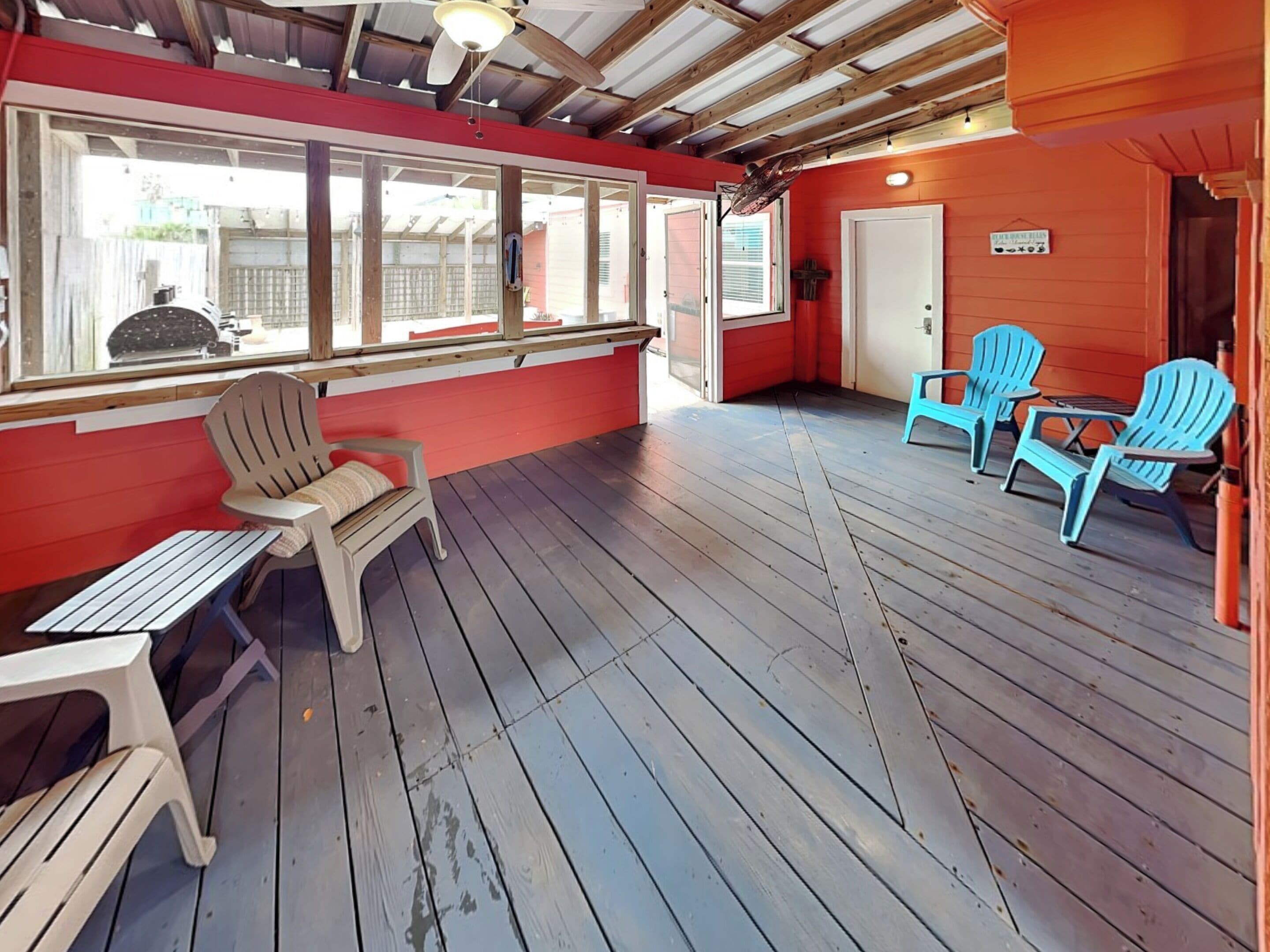 A covered outdoor area with a wooden deck, red walls, and two Adirondack chairs.