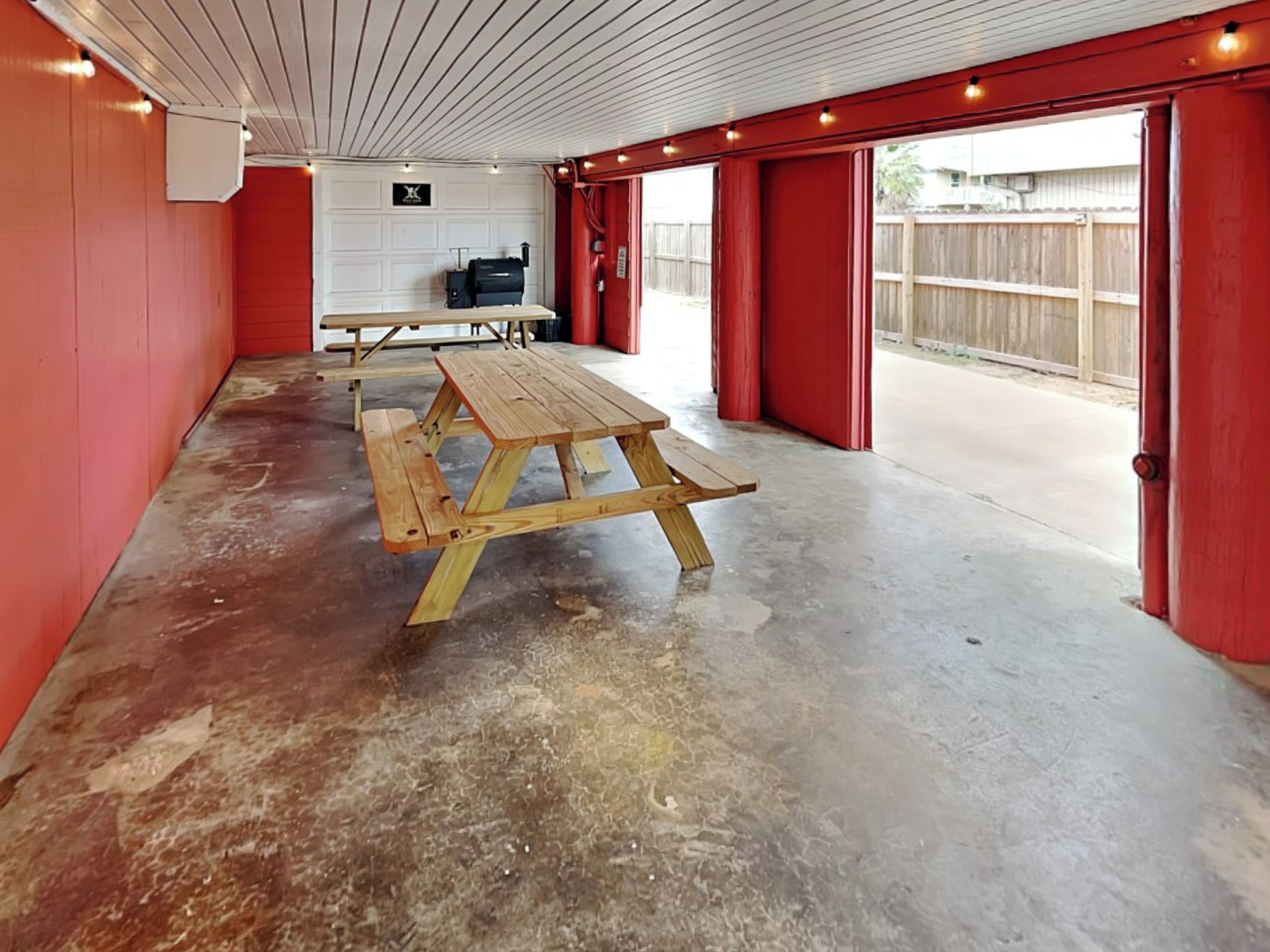 A covered outdoor area with picnic tables and a red wall.