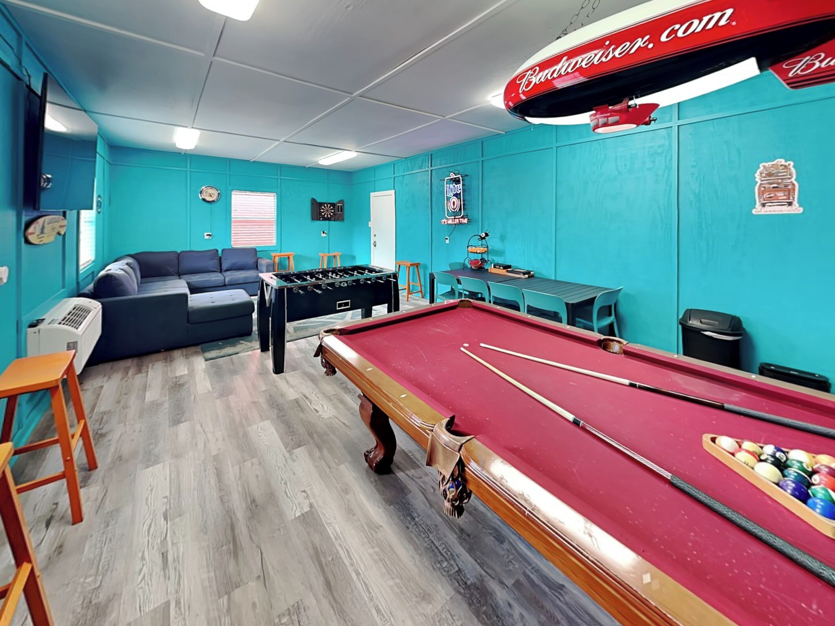 A room with a pool table, foosball table, sofa, and a table with chairs.