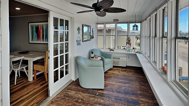 Um quarto com área de refeições, sala de estar com ventilador de teto e grandes janelas com vista para o exterior.