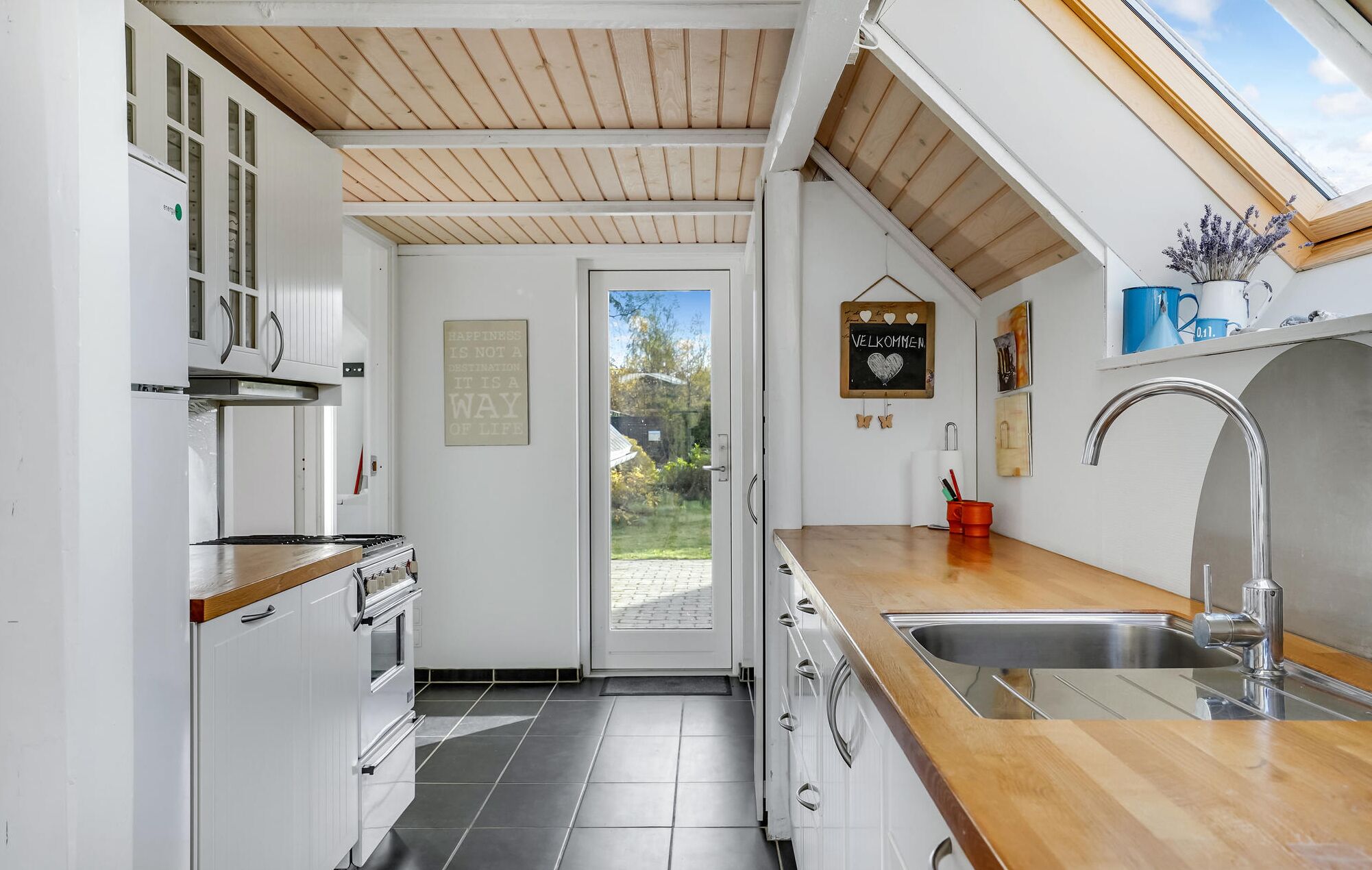 A kitchen with white cabinets, a wooden countertop, a stainless steel sink, and a skylight.