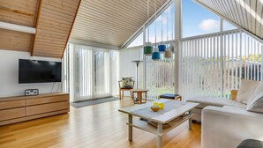 A spacious living room with a large TV, wooden flooring, and a view through floor-to-ceiling windows. - 4 bedroom amazing home in Glesborg (Glesborg)