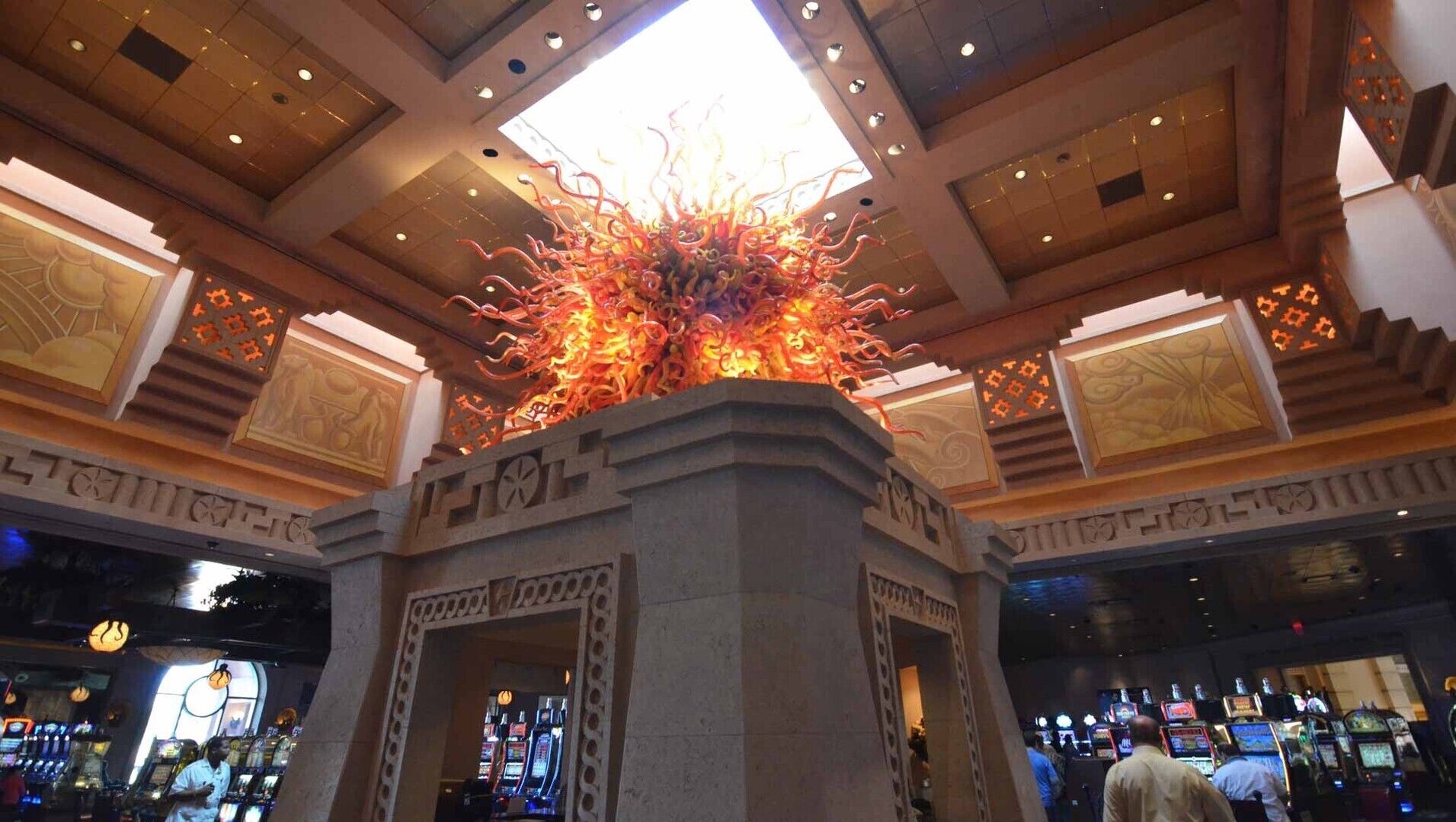 A casino interior with slot machines, a central decorative light fixture, and traditional architectural elements.