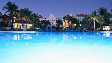 A swimming pool with lounge chairs and palm trees, surrounded by colorful buildings.
