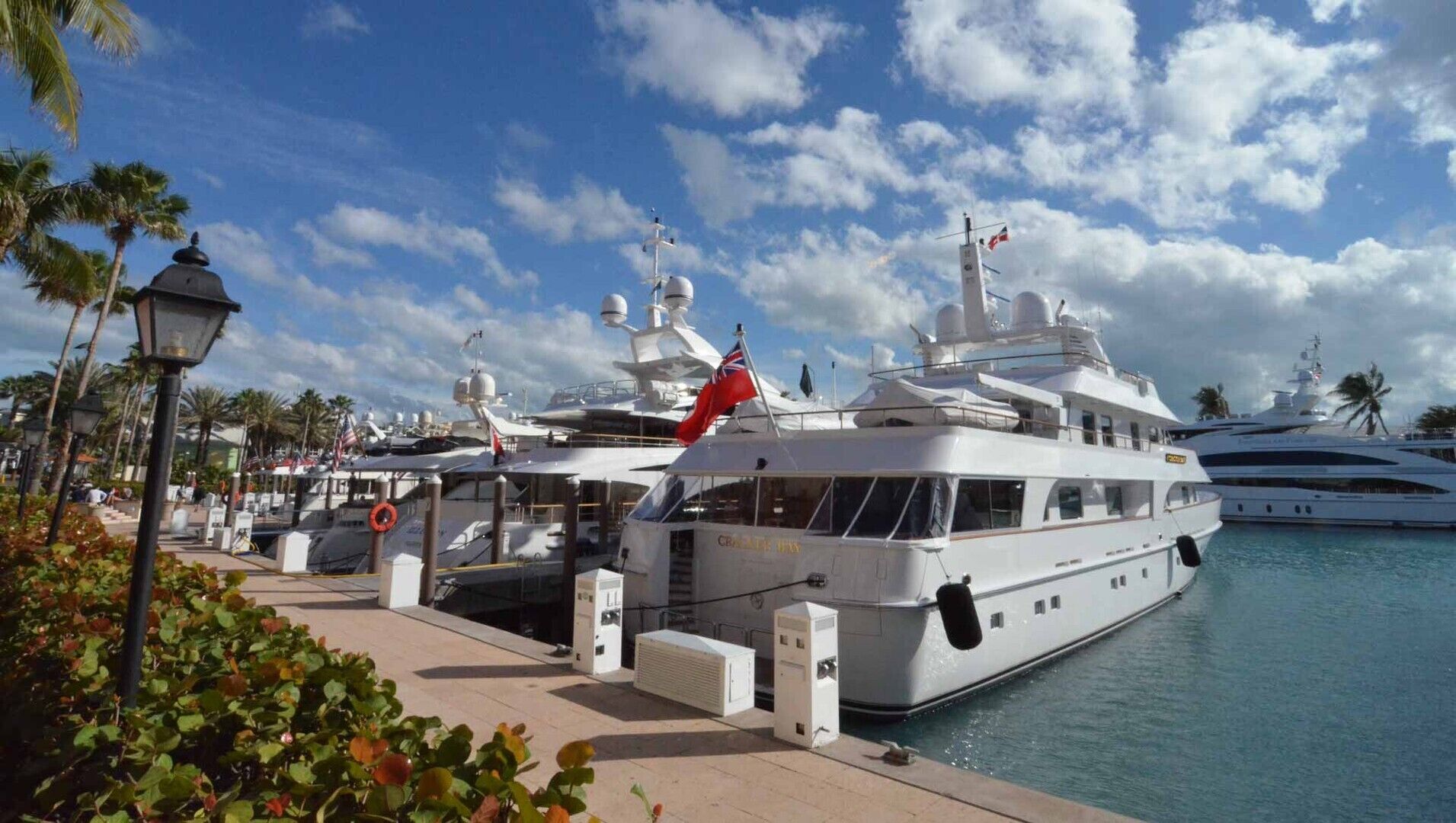 A marina with several yachts docked, featuring lifebuoys, a flag, and a clear sky.