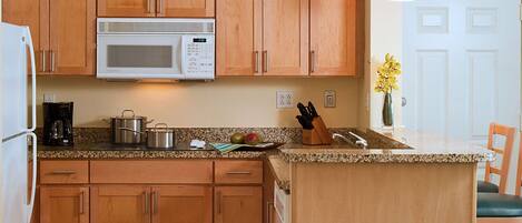 A kitchen with wooden cabinets, a microwave, a coffee maker, and a fruit bowl.