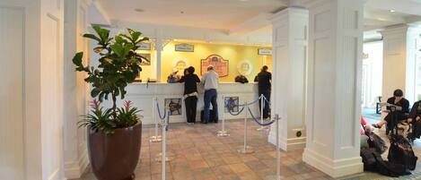 A hotel reception area with a check-in counter, a large potted plant, and a tiled floor.