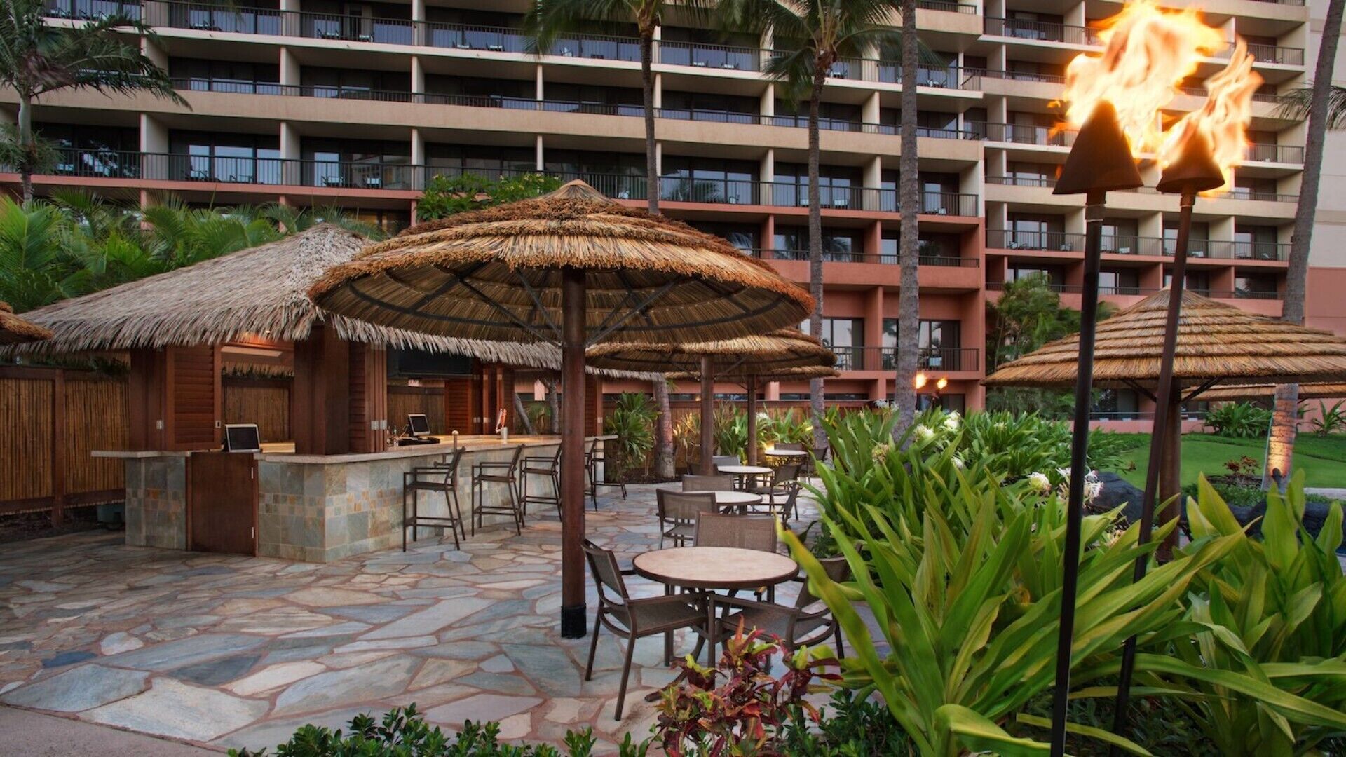 Un patio de hotel con suelo de piedra, sombrillas de paja y mobiliario para exteriores.