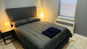 Un dormitorio con cama, mesitas de noche, una ventana con persianas y un radiador.