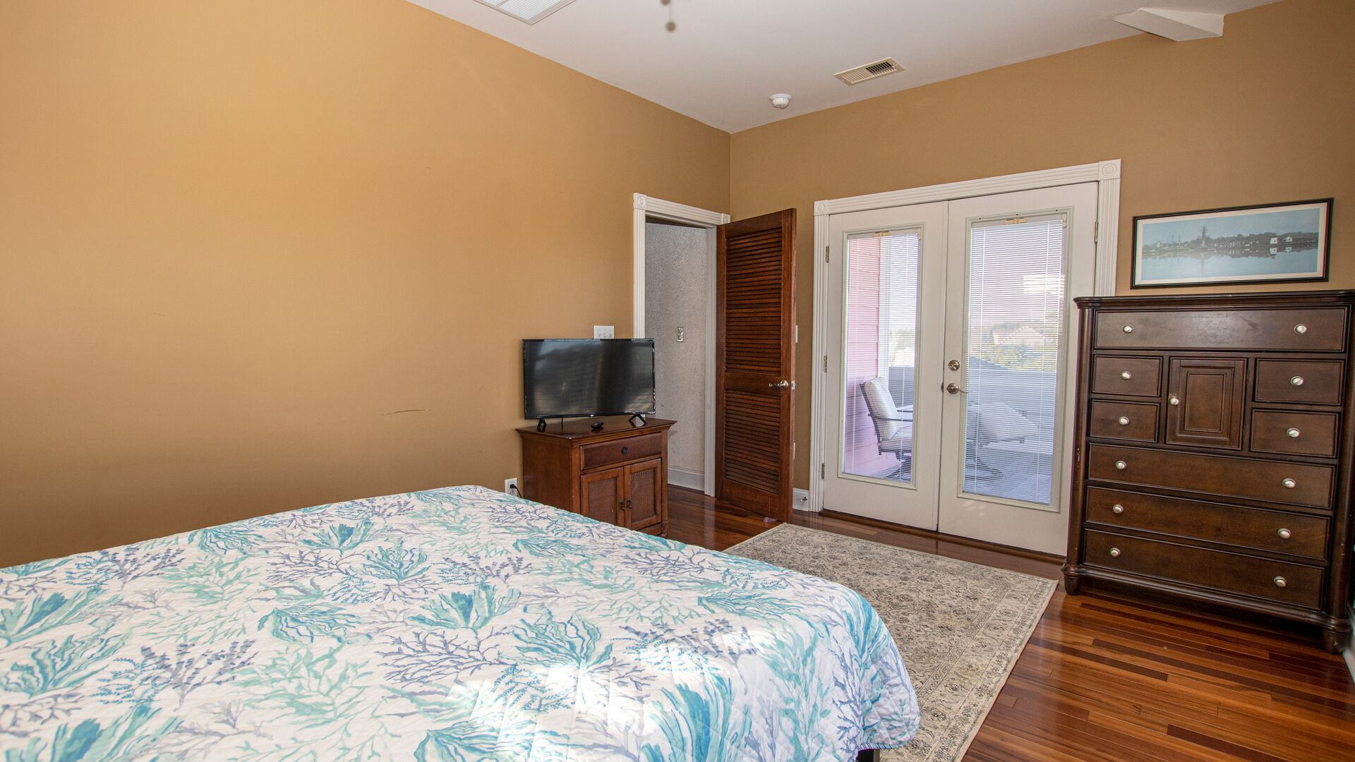 A bedroom with a bed, a dresser, a television, and a sliding glass door leading to a balcony.