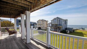 A wooden deck with white railings overlooking a grassy area and a body of water. - Soundfront, Sound Views, Private Dock, Rec Room, COL21, Warrens Sound Retreat (Kill Devil Hills)