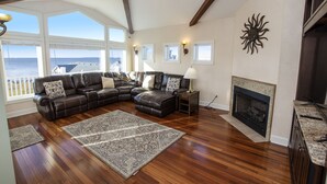 A spacious living room with a large sectional sofa, a fireplace, and a view of the ocean. - Soundfront, Sound Views, Private Dock, Rec Room, COL21, Warrens Sound Retreat (Kill Devil Hills)
