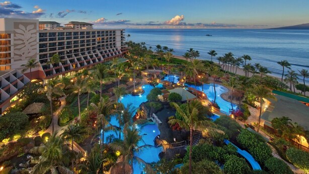 A resort with multiple swimming pools surrounded by lush greenery and palm trees, overlooking a beach and the ocean.