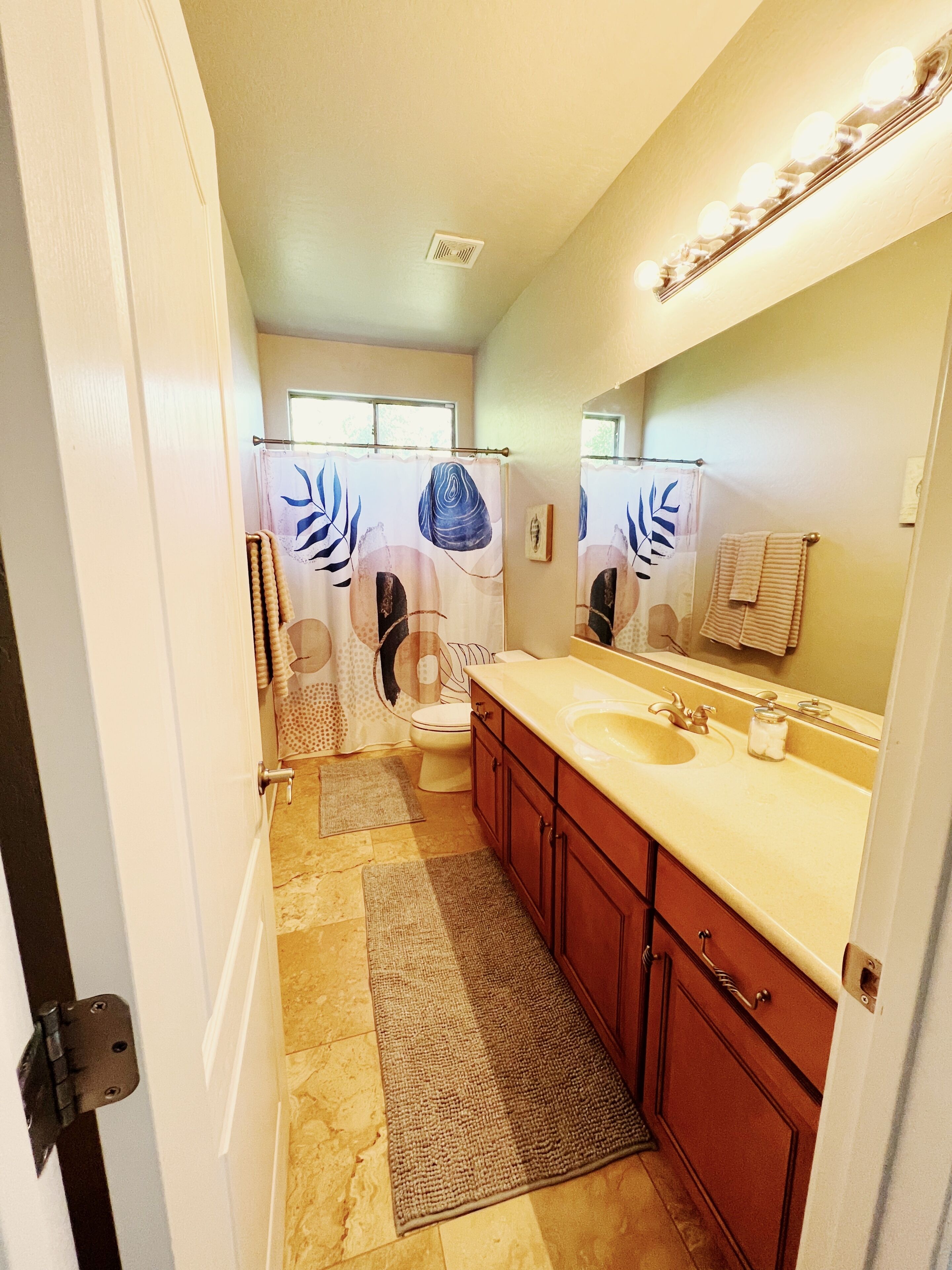 A bathroom with a beige vanity, a large mirror, and a shower curtain with a leaf pattern.