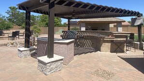 An outdoor patio with a pergola, grill, and seating area.