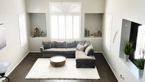 A modern living room with a grey sofa, a white rug, and a ceiling fan.