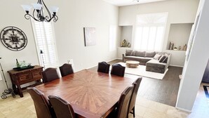 A spacious dining area with a large wooden table surrounded by chairs, a chandelier, and a dining table set with a bottle and glasses.