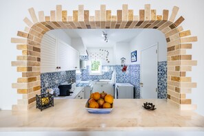 A kitchen with a brick archway, white cabinets, blue and white patterned backsplash, and a bowl of fruit on the counter. - CoolHouses Algarve Luz | Casa Isabell T1 (Luz)