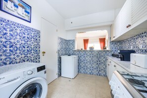 A compact kitchen with a washing machine, a small refrigerator, and a microwave. - CoolHouses Algarve Luz | Casa Isabell T1 (Luz)
