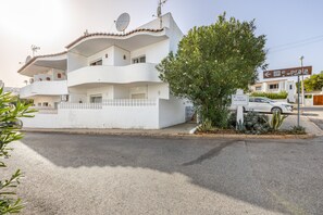 A white multi-story residential building with balconies, a satellite dish, and a sign indicating 'Praia'.