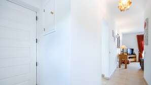 Un corridoio con una porta bianca, un tavolo in legno con una lampada e un televisore.