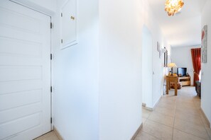 A hallway with a white door, a wooden table with a lamp, and a television set. - CoolHouses Algarve Luz | Casa Isabell T1 (Luz)