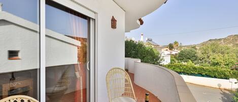 A balcony with a table, two chairs, a bottle of wine, and a view of the surrounding landscape.