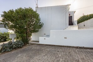 A white building with a flat roof, a small staircase leading to a door, and a tree in the foreground. - CoolHouses Algarve Luz | Casa Isabell T1 (Luz)