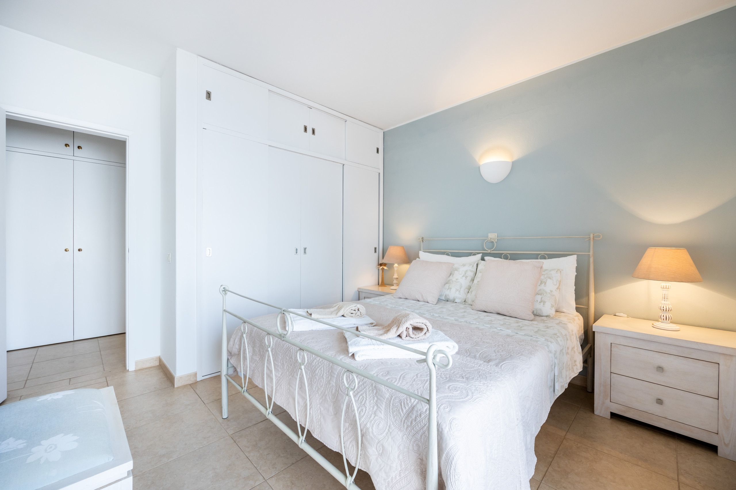 Un dormitorio con cama, mesitas de noche, armario y una lámpara fijada a la pared.