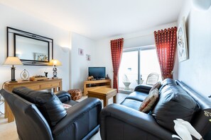 A living room with a sofa, a television, a wooden side table, and a lamp. - CoolHouses Algarve Luz | Casa Isabell T1 (Luz)