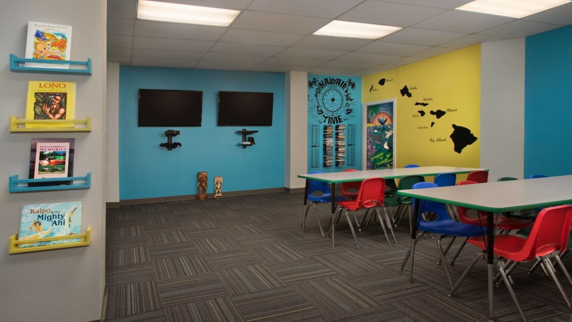 Une salle de classe aux murs bleus et jaunes, dotée d’un tapis à motifs chevrons et de chaises colorées.