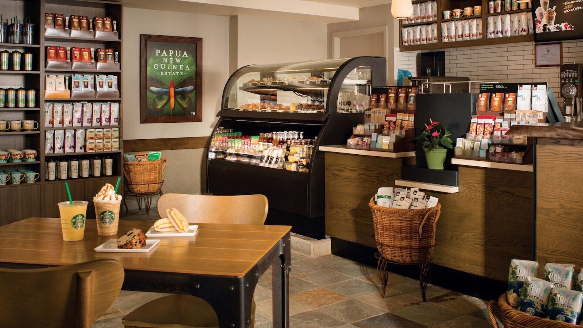 Ein Café-Interieur mit Kaffeebohnen-Auslage, einer Theke mit Gebäck und einer Sitzecke mit Tisch und Stühlen.