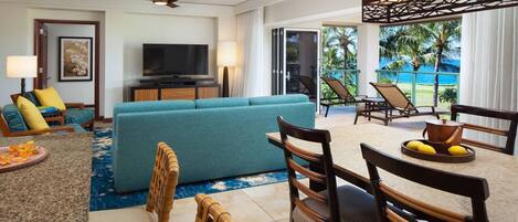 Habitación de hotel moderna con sofá, sillas, televisor y balcón con vista al océano.