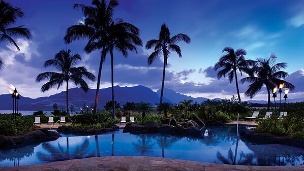 A pool area with lounge chairs, palm trees, and a mountainous backdrop.