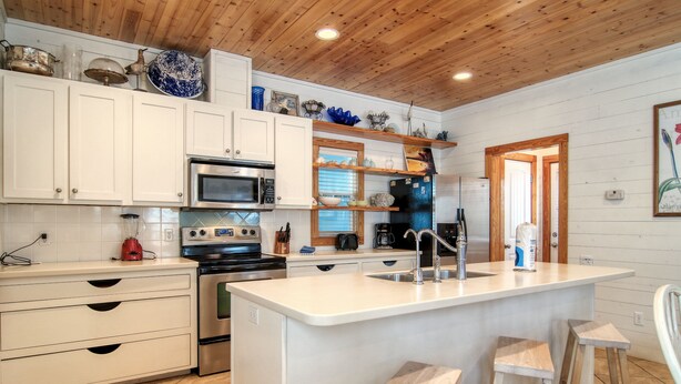 Una cocina moderna con armarios blancos, una isla central con taburetes, microondas, estufa y refrigerador.