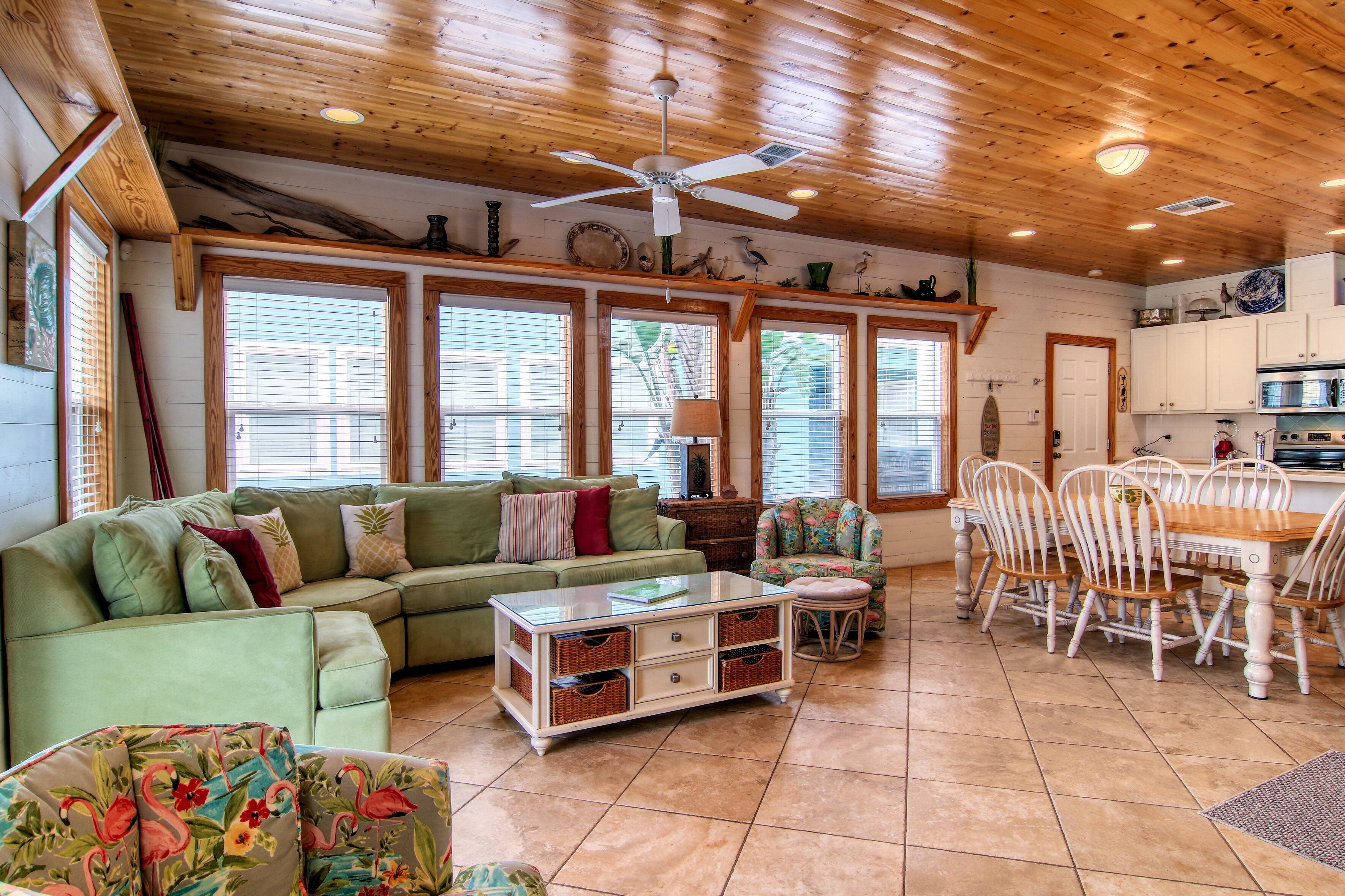 A spacious living room with a green sofa, a glass coffee table, and a dining area with a wooden table and chairs.