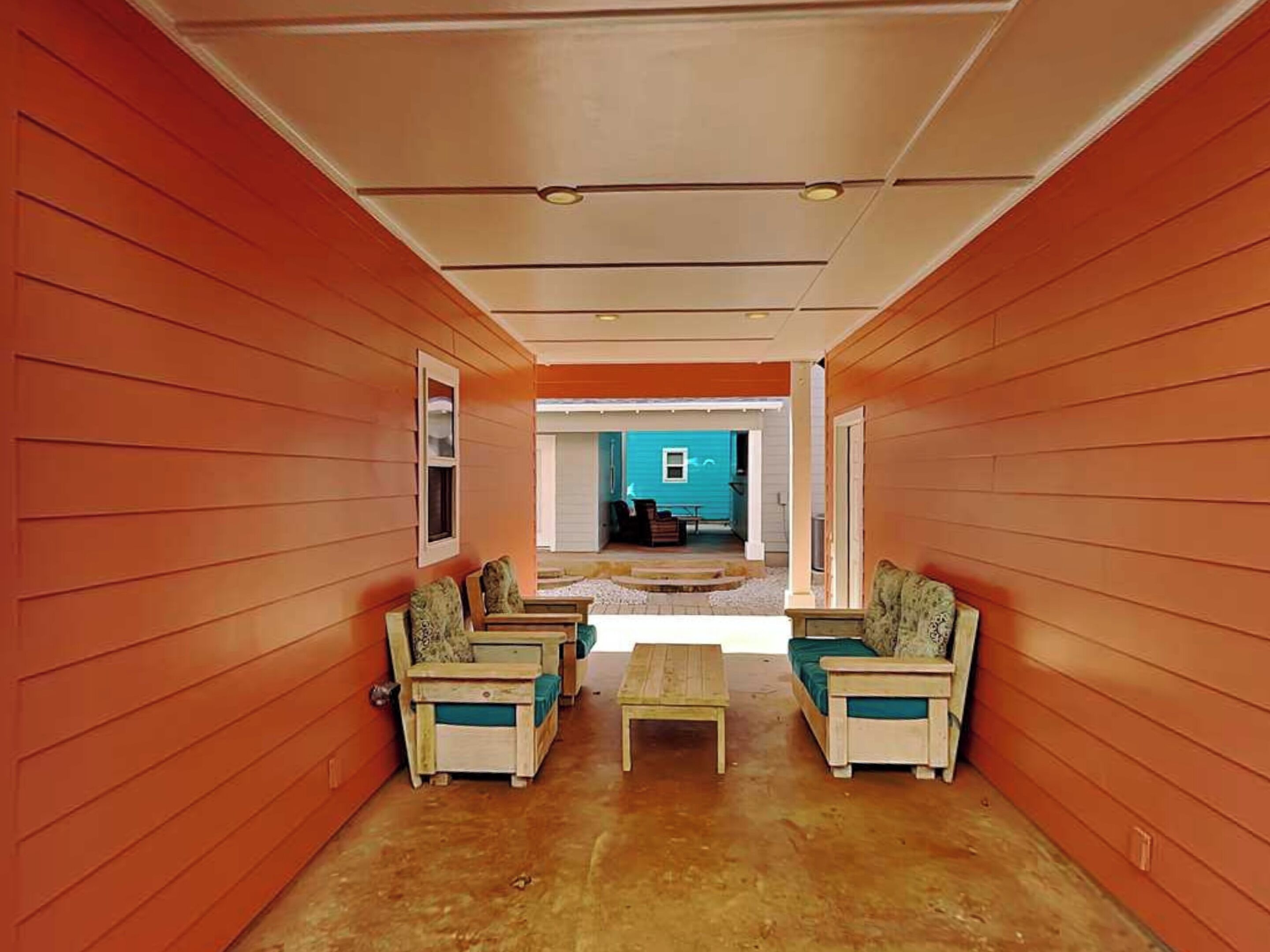 A corridor with wooden walls and a view to a blue house.