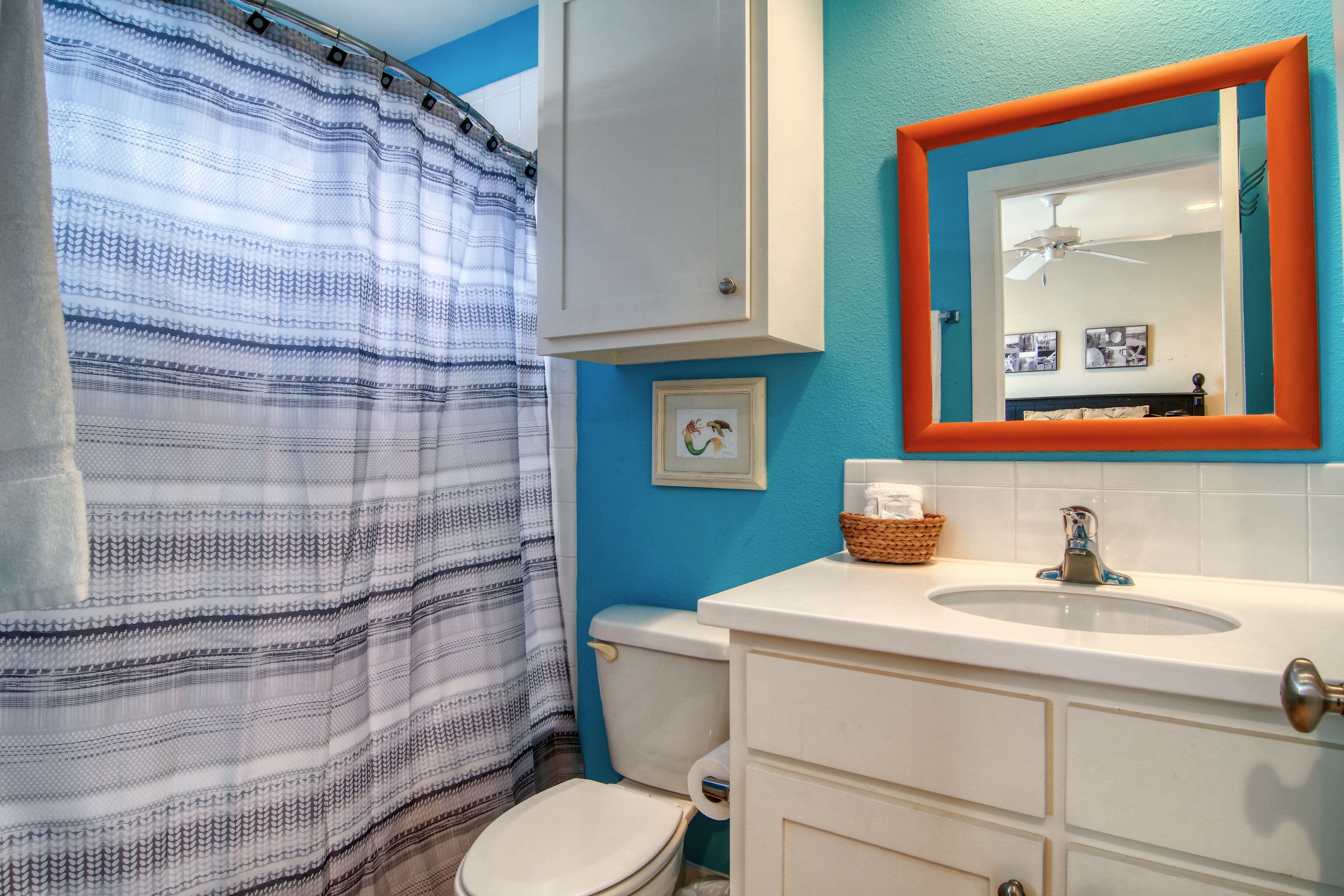 A bathroom with a striped shower curtain, a white toilet, a white sink with a mirror, and a ceiling fan.
