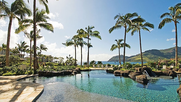 A resort pool area with clear water, surrounded by palm trees and a view of the ocean and mountains. - Ocean View - 3 Bedroom - Marriott's Kauai Lagoons - Full Resort Access (Lihue)