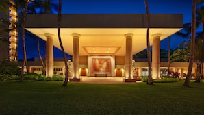 Una imponente entrada de hotel con un amplio mural central, columnas simétricas y un césped bien cuidado.