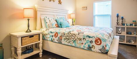 A bedroom with a bed, nightstands, a decorative wall, a window, and a shelf with items.