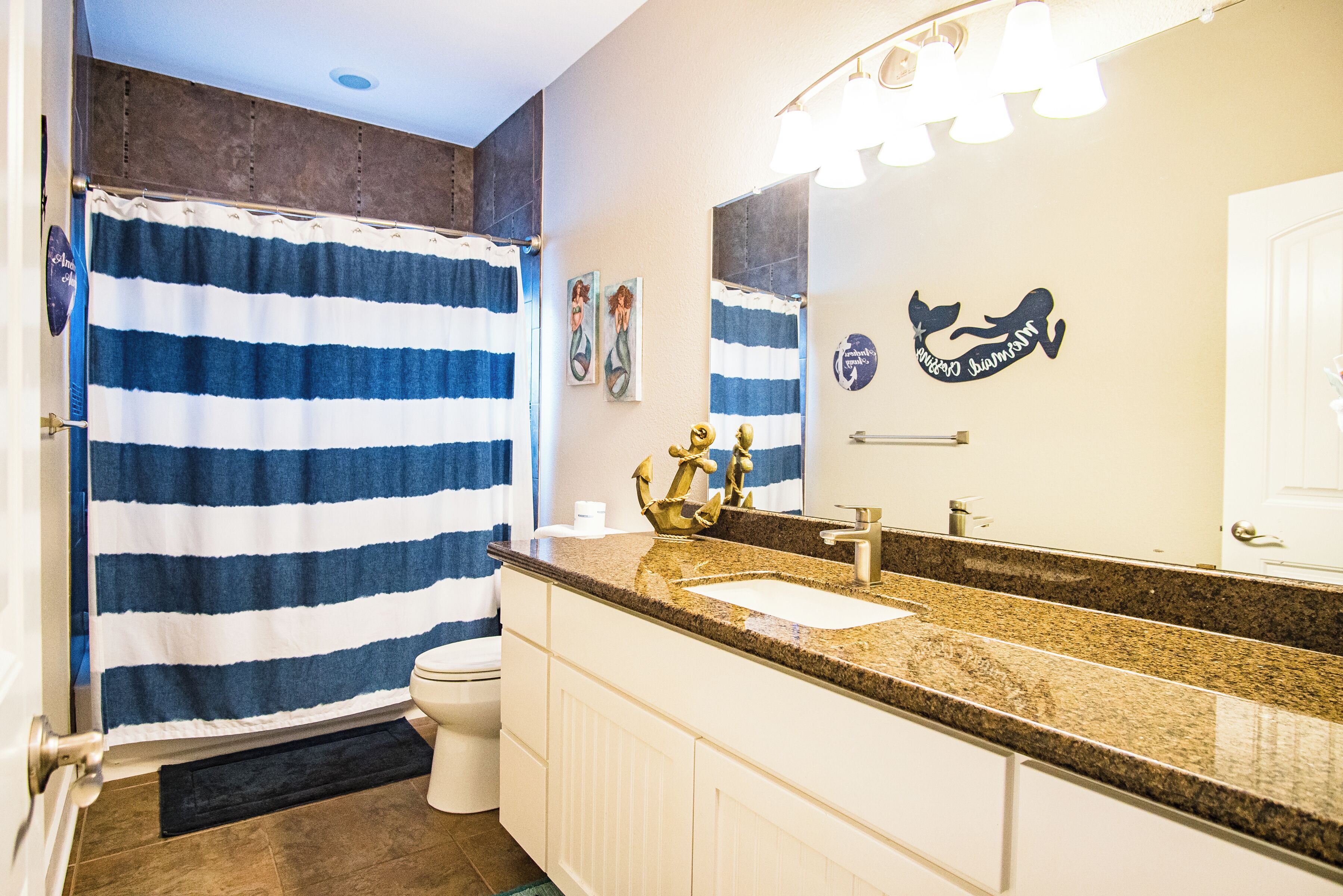 Une salle de bain avec un rideau de douche à rayures, un lavabo avec un robinet doré et un miroir orné d’une tête de baleine décorative.