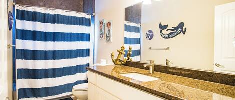 Une salle de bain avec un rideau de douche à rayures, un lavabo avec un robinet doré et un miroir orné d’une tête de baleine décorative.